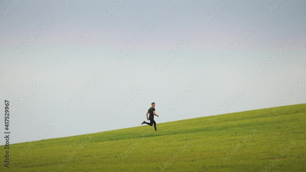 The sportsman is quickly running across the green grass. He is running down the slope. Running training. 4K. The sportsman is quickly running across the green grass. He is running down the slope. Running training. 4K.