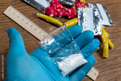 evidence of smuggling traffic: Packaging of a narcotic substance in the hand of a forensic expert against the background of other arrested materials, cocaine, heroin, spice