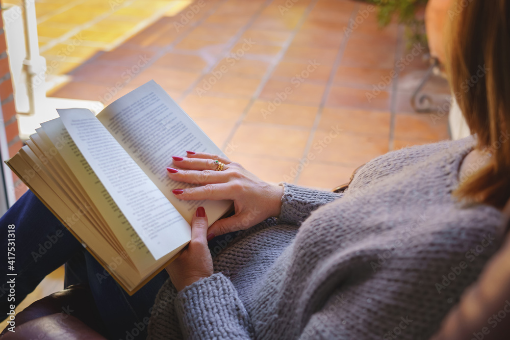 Obraz premium White woman reading a book in an armchair relaxing in nice daylight outside. Copy space. Reading, teaching concept.