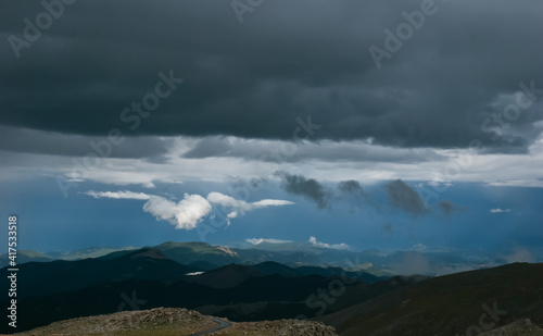 Colorado Rocky Mountain vista of low hanging clouds against a dark sky above a highlighted mountain top and lake as viewed from Mount Evans Highway  Colorado USA