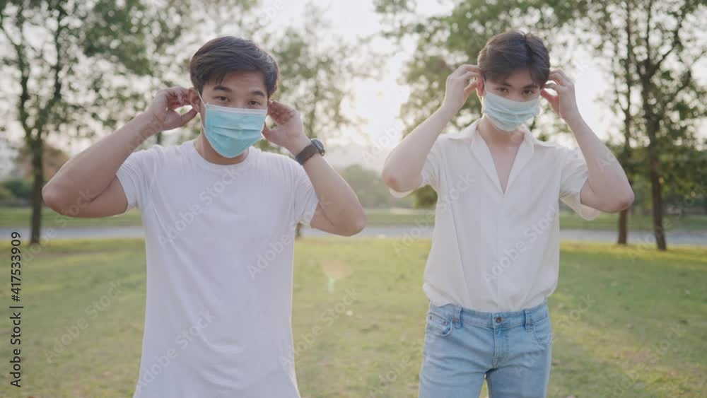 Young asian men friends put on protective face mask protecting themselves from transmitted infectious diseases virus, young adult wear medical face mask standing inside the park new normal distancing Young asian men friends put on protective face mask protecting themselves from transmitted infectious diseases virus, young adult wear medical face mask standing inside the park new normal distancing