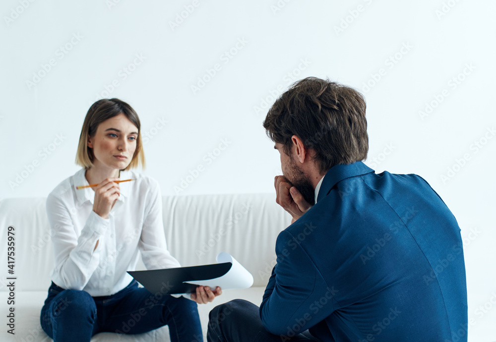 A business man in a suit is gesturing with his hands and a woman is sitting on the couch