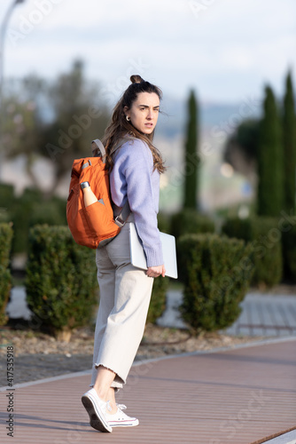 Full body portrait of a pretty entrepreneur looking back while she is walking in a park. © Egoitz