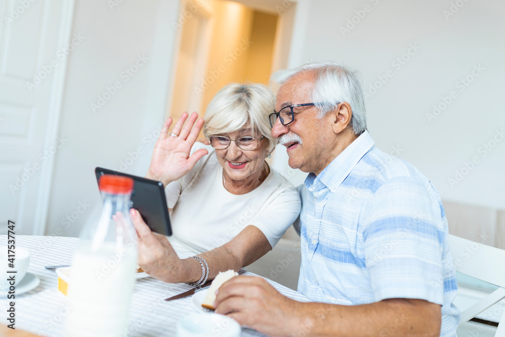 Senior man and his wife are using a digital tablet and communicating with their kids. Happy senior couple is having breakfast and having an online conversation with their family and sending greetings. Senior man and his wife are using a digital tablet and communicating with their kids. Happy senior couple is having breakfast and having an online conversation with their family and sending greetings.