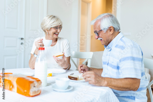 Happy senior couple having breakfast at home. Elderly couple smiling to each other. Old couple having fun during breakfast. Food, eating, people and healthy food concept