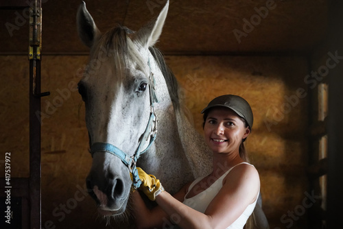 Young woman wearing riding gloves on hand standing near horse inside stables
