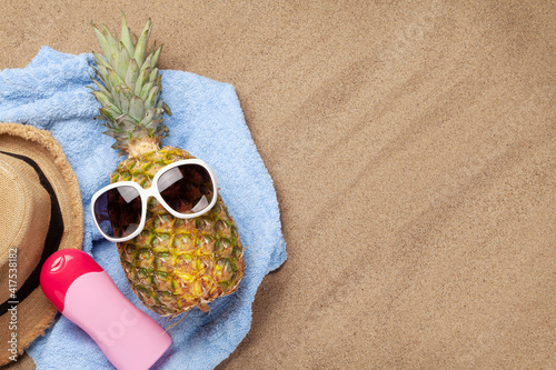 Pineapple with sunglasses on hot sand beach