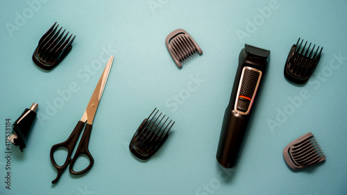 Professional hairdressing tools, hair clipper with attachments and scissors on a blue background.