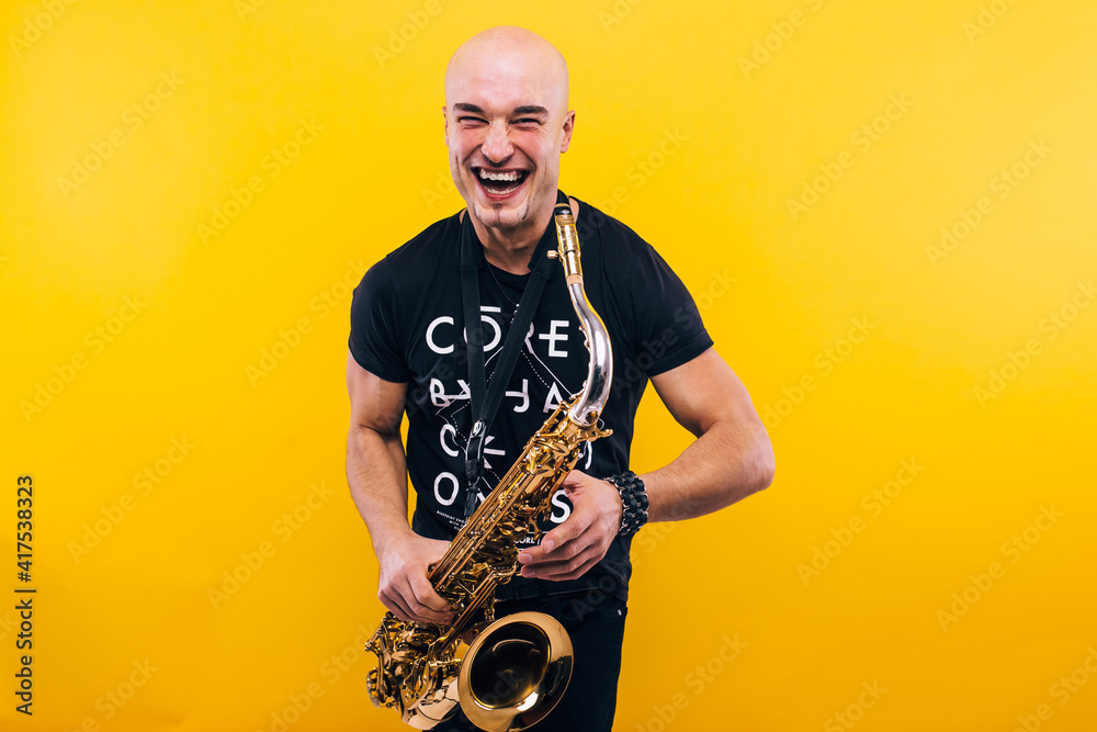 Fototapeta premium A man holding a saxophone in the studio against a yellow background