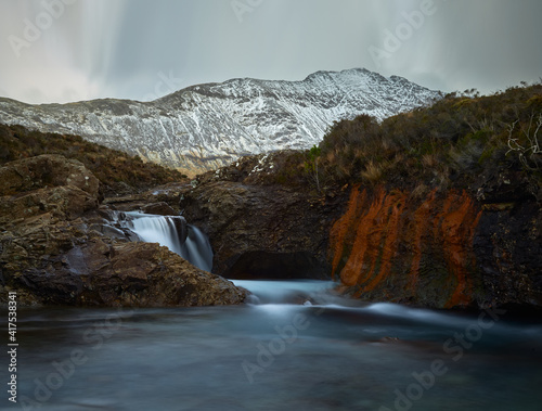 turquoise and idilyc water with rocks and silky water. red cliff and wintes mountains - Fairy Pools - Skye Island - Scotland - Uk