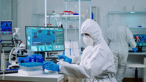 Doctor with protection suit working with blood samples in laboratory typing on computer. Chemist examining vaccine evolution using high tech for research in treatment development against covid19 virus