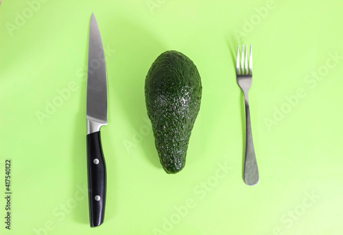 A whole avocado is on the table and a fork and knife are next to it. The concept of dietary proper nutrition. photo