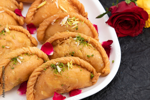 Gujia Or Gujiya Mithai Made In Desi Ghee Dry Fruits Pista Badam Kesar Is Mostly Enjoyed On Festivals Like Happy Holi Diwali Rakshabandhan Deepawali Eid In India. Rose Petals Decor On Black Background photo