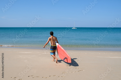 A sportman man with paddleboard going to the sea having fun and enjoying their vacations outdoors at the beach of Thailand. Surfer lifestyle. SUP or Stand Up Paddle Boarding.