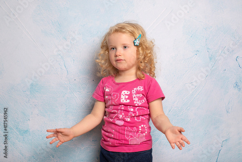 Portrait of a cute little curly blonde 2 year old girl of blue background