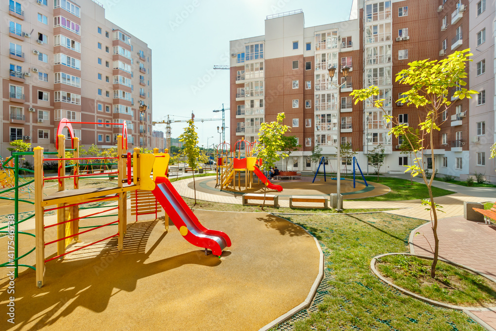New modern colorful children playground in sunny summer green courtyard among residential high-rise buildings New modern colorful children playground in sunny summer green courtyard among residential high-rise buildings