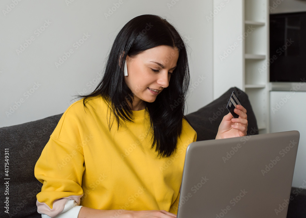 Beautiful brunette freelancer is shopping online at home with a credit card and laptop. Shopping during quarantine, pandemic content Beautiful brunette freelancer is shopping online at home with a credit card and laptop. Shopping during quarantine, pandemic content