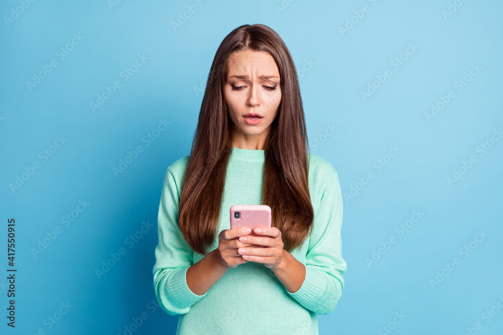 Portrait of lovely focused sullen brown-haired girl using gadget browsing bad news media isolated over bright blue color background Portrait of lovely focused sullen brown-haired girl using gadget browsing bad news media isolated over bright blue color background