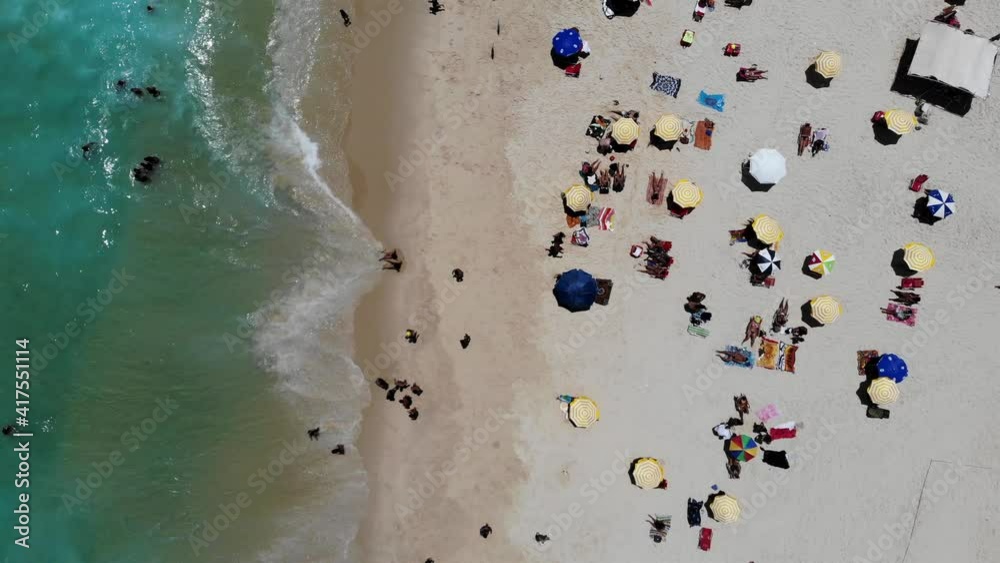 top view of Drone flying downwards in Barra da Tijuca beach while waves crash on beach. morning traffic near noon, lots of people on the beach on beautiful sunny day