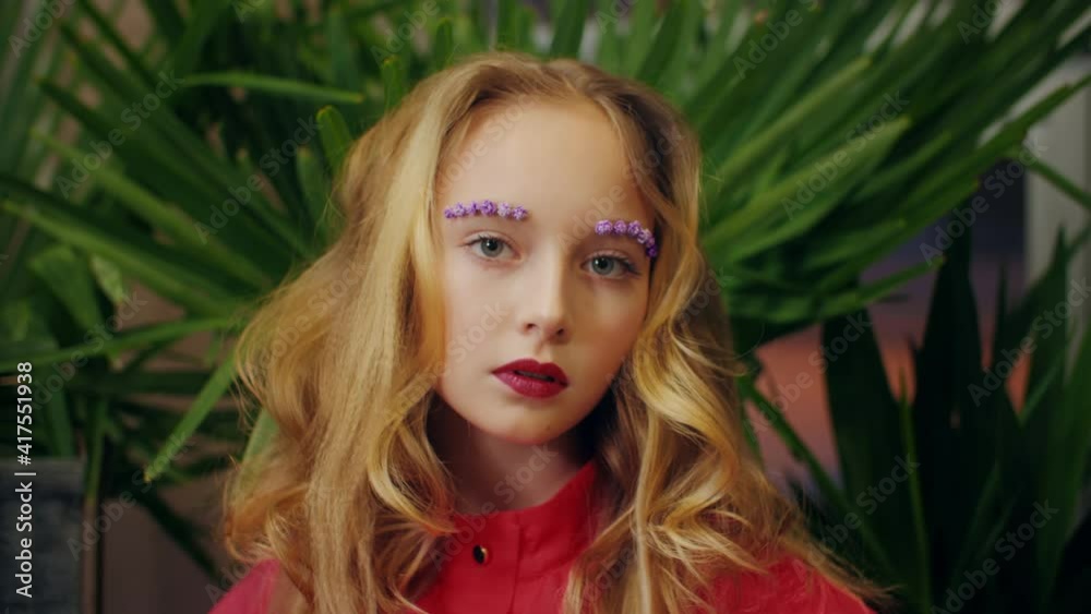 Portrait fashion girl with flower makeup and curly hairstyle posing front camera in orangery. Beautiful model with fashion make up looking to camera Portrait fashion girl with flower makeup and curly hairstyle posing front camera in orangery. Beautiful model with fashion make up looking to camera