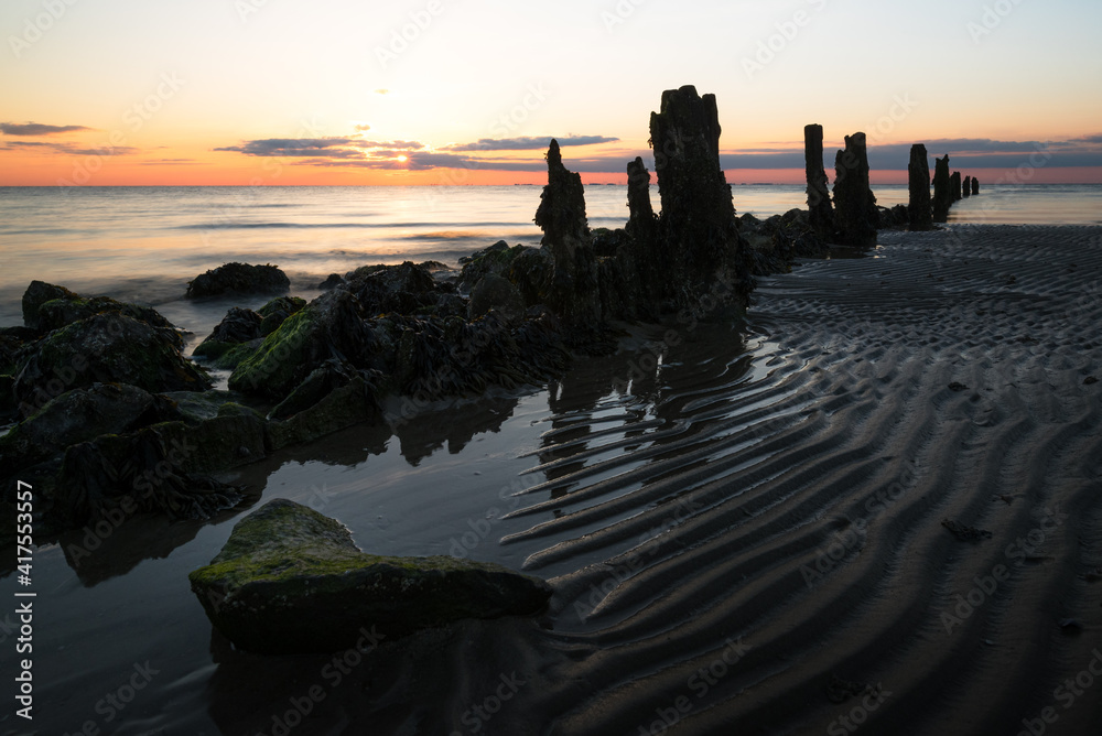 Rocks and poles with rising tide at a scenic beach on Sylt island Germany during a beautiful sunrise
