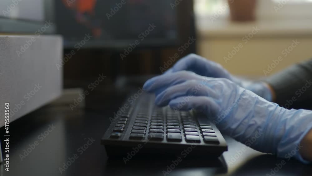 Typing at keyboard with surgical gloves during Coronavirus lockdown. rubber-gloved hands typing on eng-rus keyboard, tender woman hands, dark background. precautions during pandemy. Close up Typing at keyboard with surgical gloves during Coronavirus lockdown. rubber-gloved hands typing on eng-rus keyboard, tender woman hands, dark background. precautions during pandemy. Close up