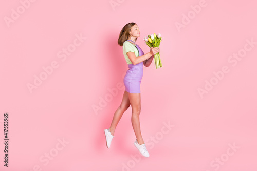 Full length body size photo of schoolgirl jumping smelling flowers bunch scent enjoy dreamy isolated pastel pink color background