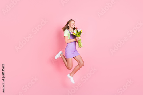 Full length body size photo of little girl jumping with tulips bunch laughing happy isolated pastel pink color background