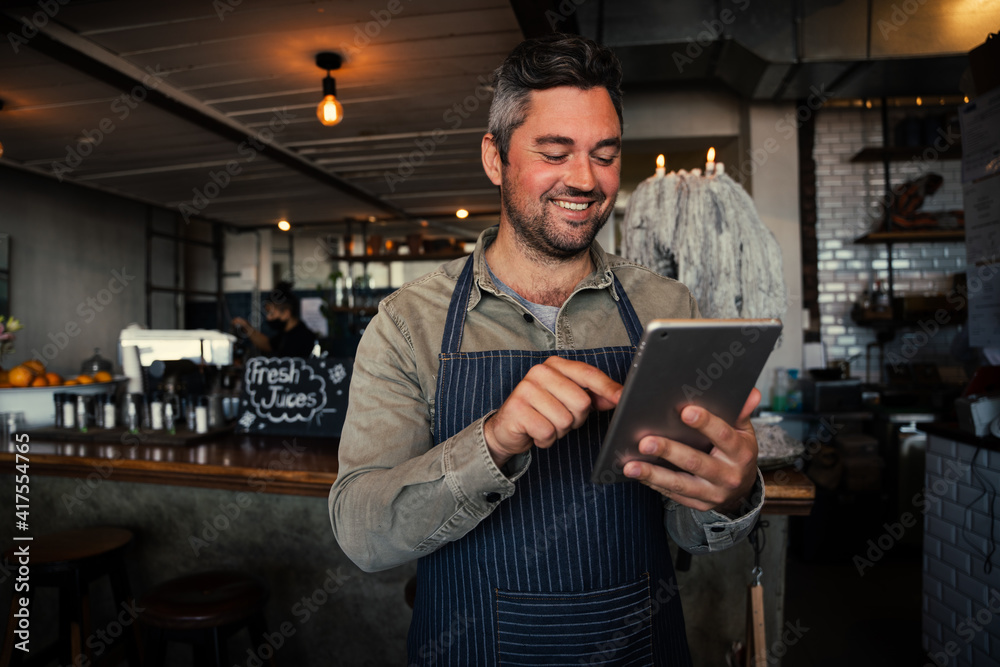 Male waiter smiling while receiving monthly salary on digital tablet in trendy cafe 