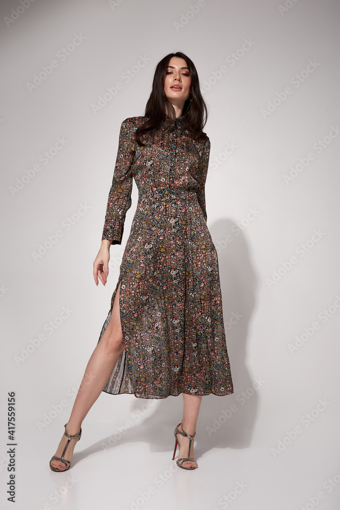 Fototapeta premium Beautiful brunette woman tanned skin glamour model pose wear fashion clothes midi long silk dress style for date party meeting work and high heels shoes accessory jewelry catalog studio background.