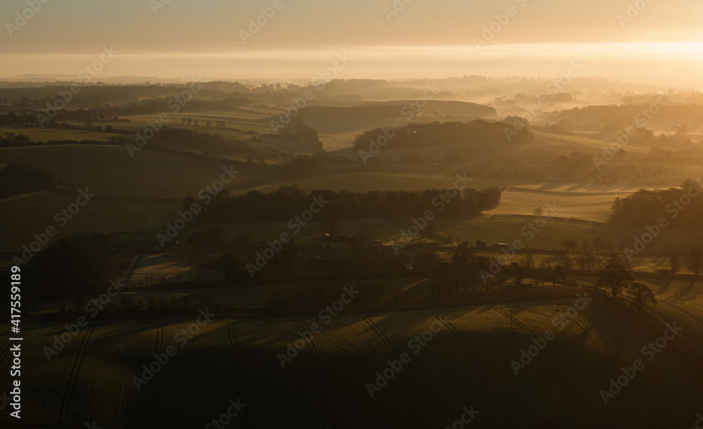 Fototapeta premium sunrise casts a golden glow on the rising mist filled Pewsey Vale from Martinsell Hill, Wiltshire