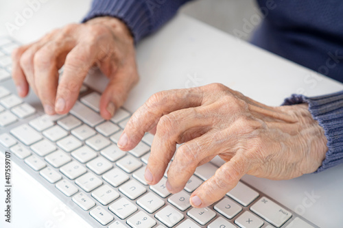 Elderly woman wrinkled hands typing on computer keyboard