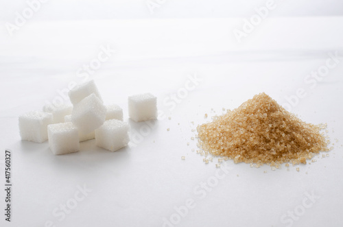 Closeup of white sugar cubes and heap of brown sugar on the white surface