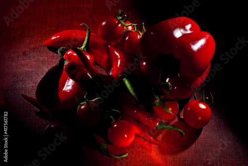 Chili peppers, bell peppers and tomatoes on a wooden board. Contrasting dramatic light as an artistic effect.