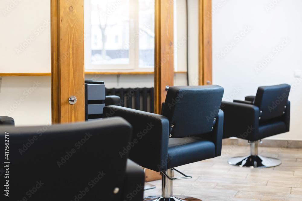 Beauty salon barbershop interior. Comfortable black leather armchairs in front of large panoramic mirrors in stylish wooden frames in a modern, cozy and bright room.