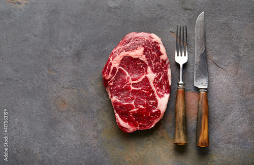 Ribeye steak with fork and knife on graphite background