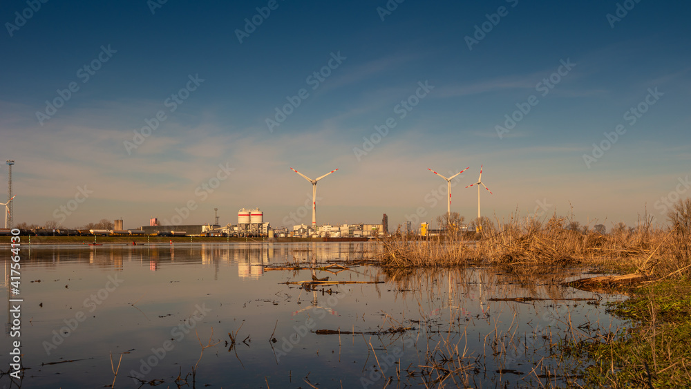 Panoramic view over Elbe riverside landscape with big wind turbines to generate electrical power as green ecofriendly energy and industrial plant at warm sunset colors, Magdeburg, Germany.