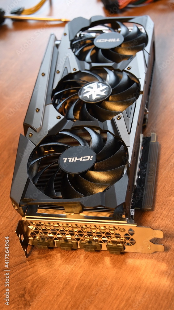 Brand new NVidia GeForce RTX 3080 graphics card for gaming PC. Three black  fans of video card cooling system with blurred wood background. Vertical  shot of gamers hardware. Illustrative Editorial Stock Photo