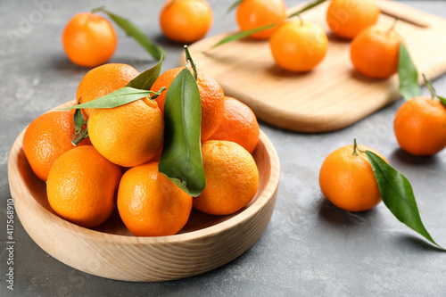 Fresh tangerines with green leaves on grey table, closeup