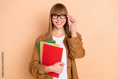 Photo of nice happy charming young woman hold notebooks wear glasses isolated on pastel beige color background