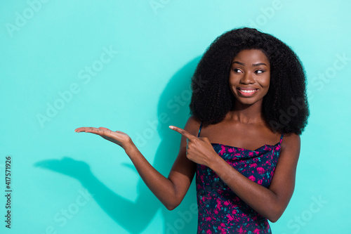 Photo portrait of curious girl smiling looking showing finger holding copyspace isolated on vibrant teal color background