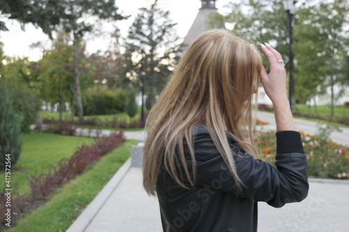Blond haired outdoor fixed her hair. She wearing black leaser jacket. Side view.