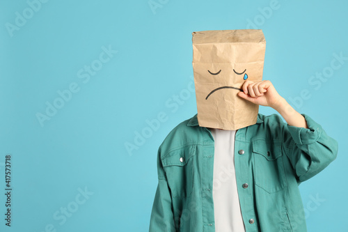 Bild auf Leinwand Woman wearing paper bag with drawn sad face on light blue background