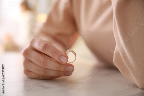 Woman holding wedding ring at table indoors, closeup. Divorce concept