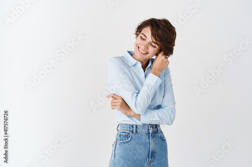 Happy authentic woman touching hair strand, smiling and looking aside with carefree face, standing on white background