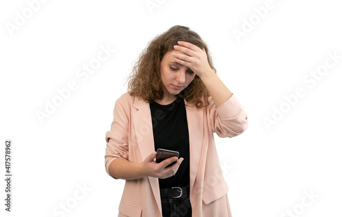 Worried woman puts her hand to head while looking at phone on white background.