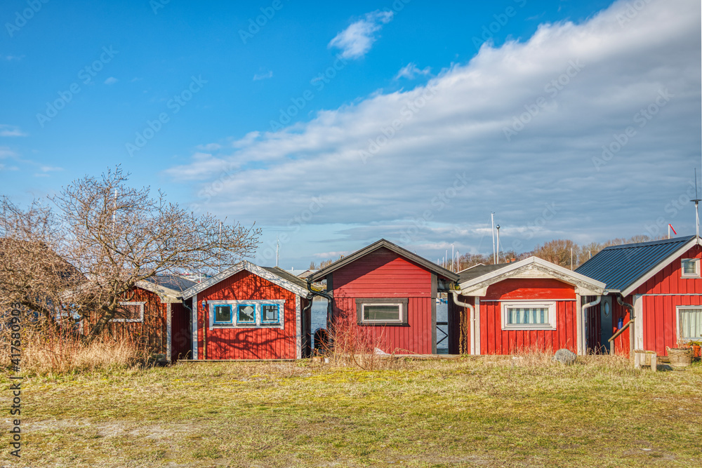 Red, traditional Swedish sommarstuga (summerhouses) or holiday houses in a sea village. Scandinavian stuga in a row by the sea account for the concept of mysig or hygge, meaning cosiness and warmth Red, traditional Swedish sommarstuga (summerhouses) or holiday houses in a sea village. Scandinavian stuga in a row by the sea account for the concept of mysig or hygge, meaning cosiness and warmth