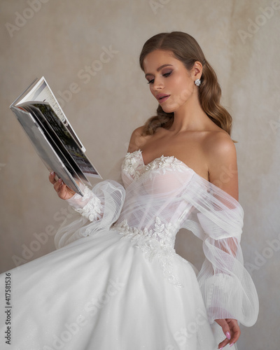 Young sylish bride with perfect make-up and hairstyle sitting in white wedding bridal dress and reading magazine photo