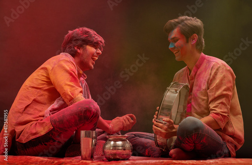 TWO FRIENDS HAPPILY LAUGHING TOGETHER AND PLAYING DAFLI DURING HOLI FESTIVAL	 photo