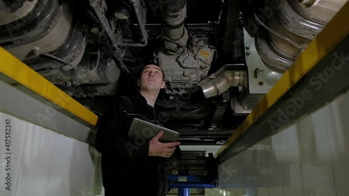 Auto mechanic makes an inspection of truck at service station. inspector records all breakdowns and problems with car in tablet. Auto service and repair cars. engineer works under car lifting machine